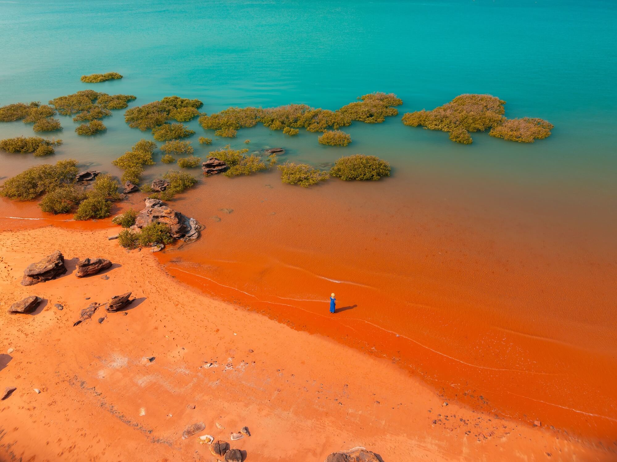 Aerial view of turquoise waters and red sand beach with mangroves