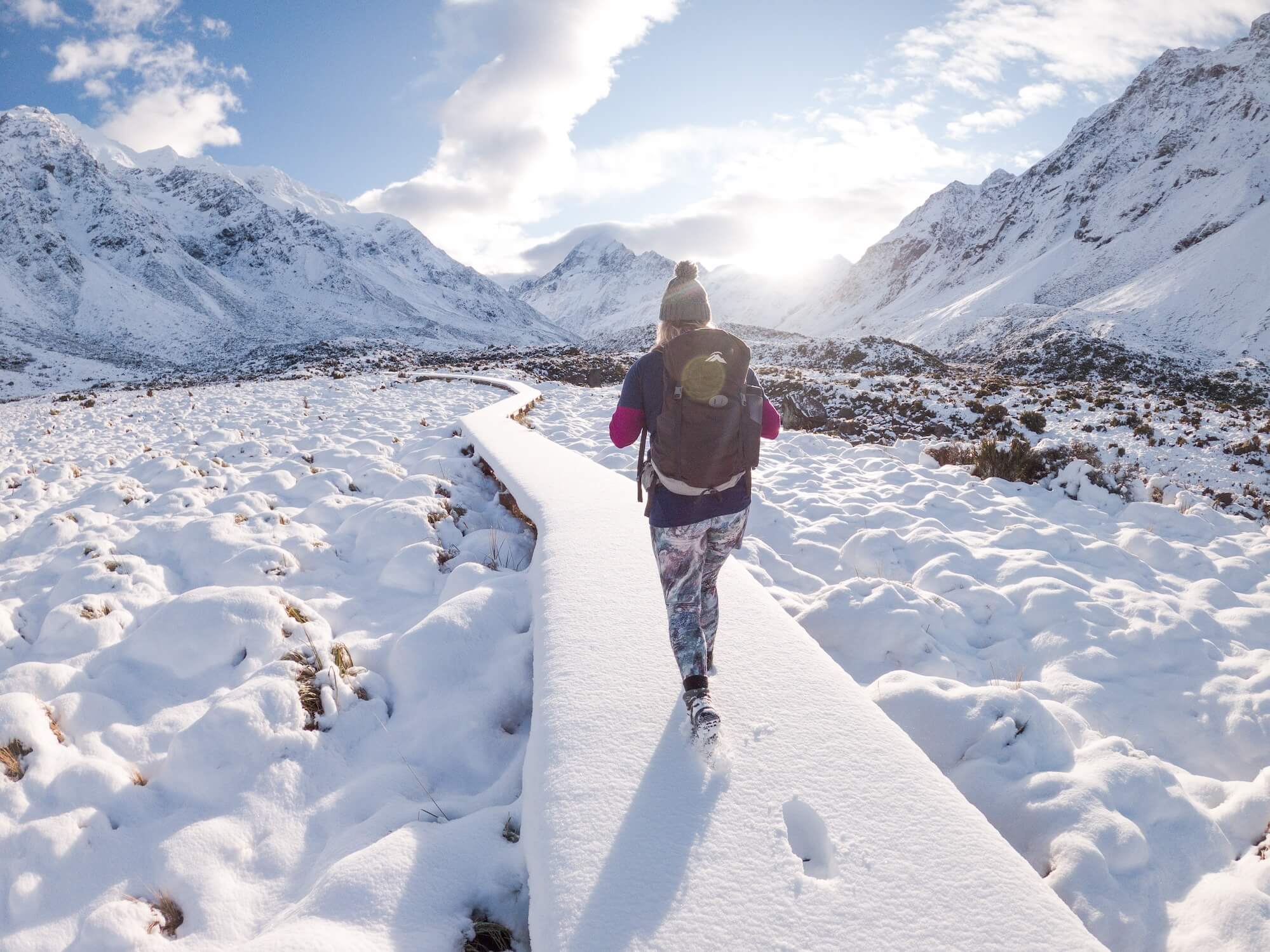 Winter hiker with backpack walking on snowy mountain boardwalk